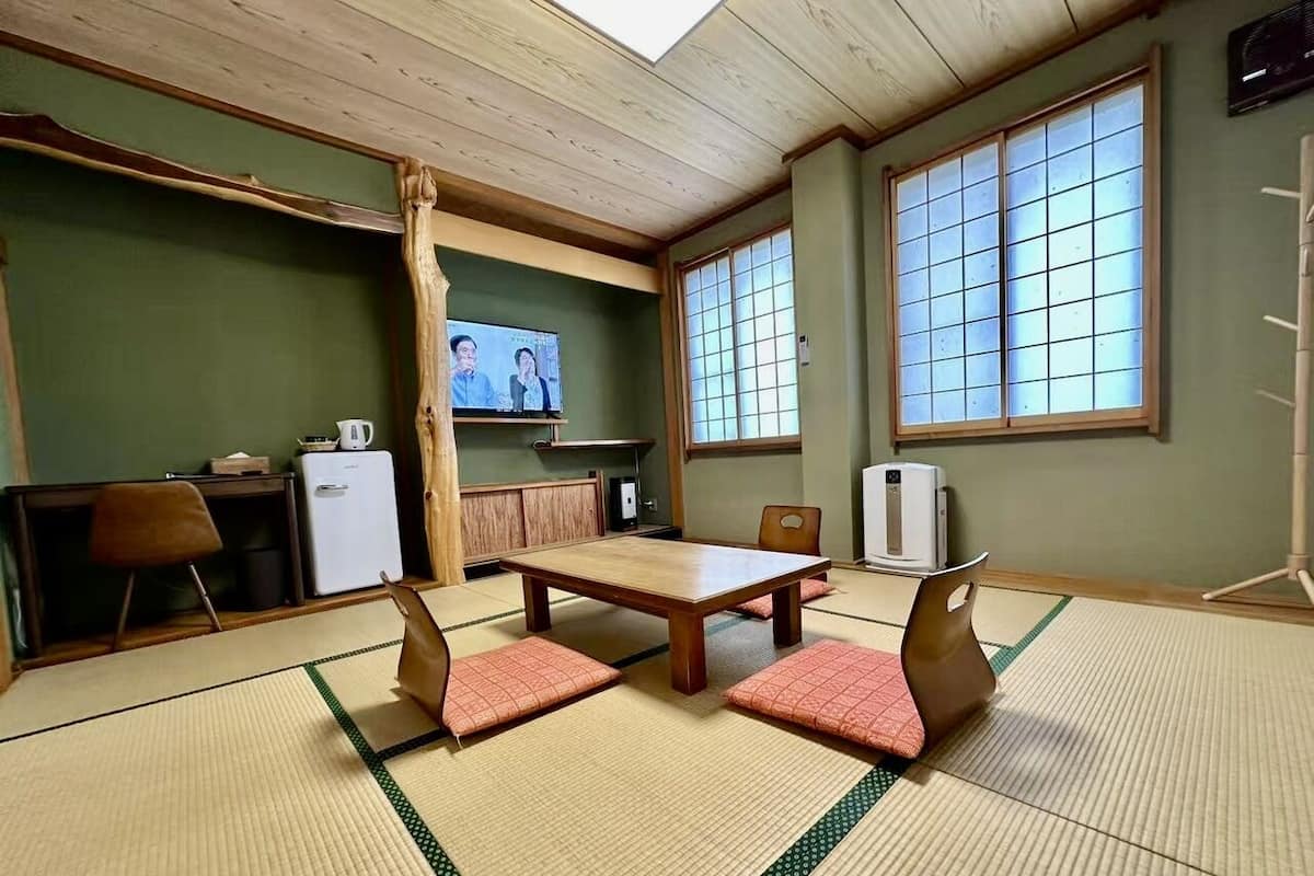 Une pièce avec un sol recouvert de tatamis, une table et des chaises en bois, un téléviseur et une fenêtre de style japonais traditionnel.