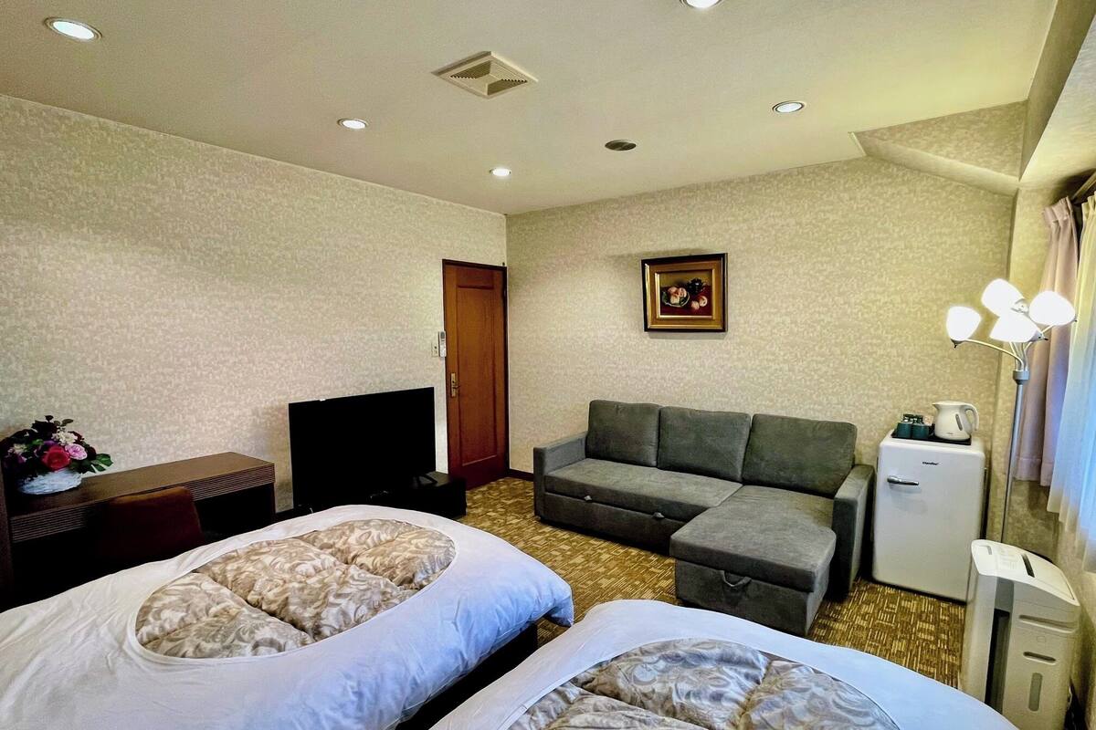 Ein Hotelzimmer mit zwei Betten, einem Sofa, einem Fernseher, einem Kühlschrank und einem Bild an der Wand.