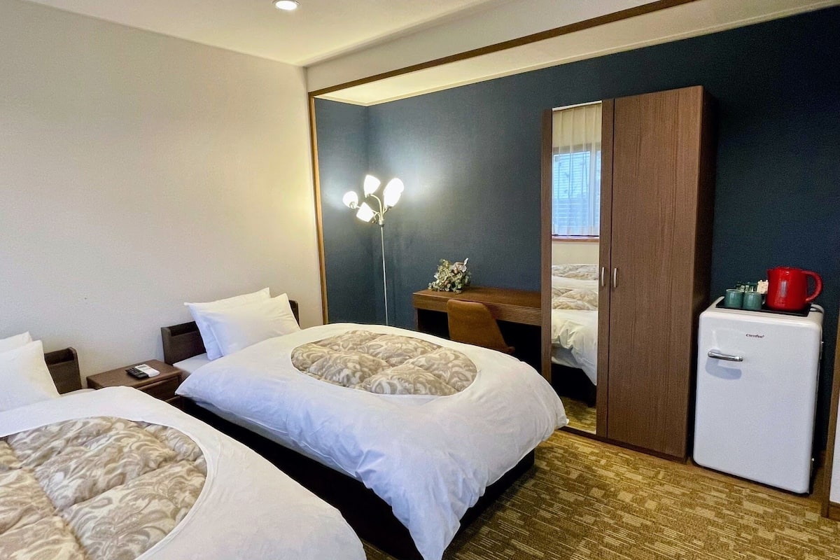 Ein Hotelzimmer mit zwei Betten, einem Schreibtisch, einem Kleiderschrank und einem kleinen Kühlschrank.