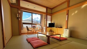Een traditionele Japanse kamer met tatami vloerbedekking, een lage tafel, twee stoelen, een televisie en een koelkast.