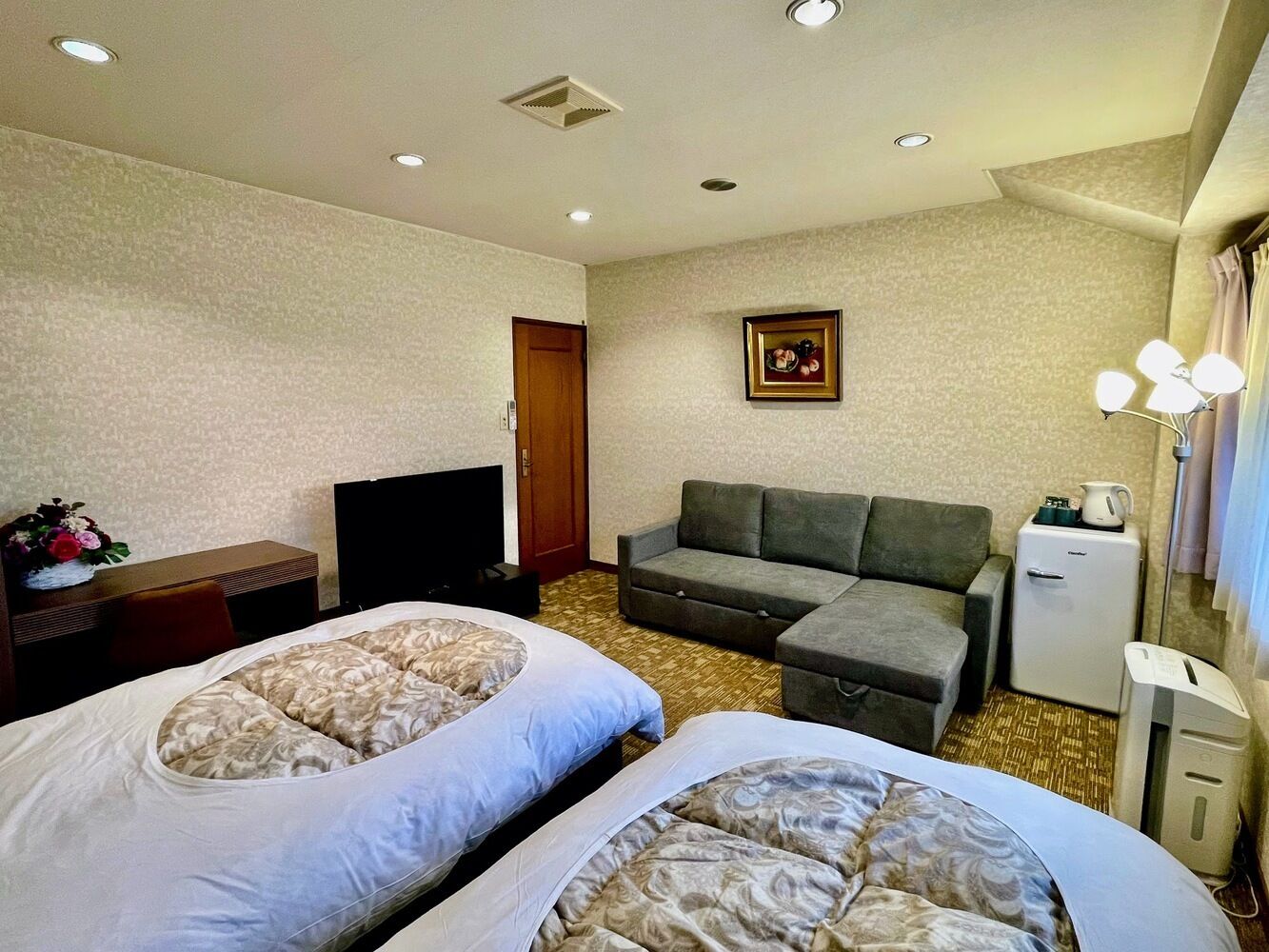 Une chambre d’hôtel avec deux lits, un canapé, une télévision, un petit réfrigérateur et un bureau avec une chaise.