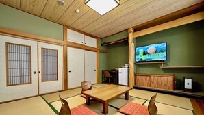 Een traditionele Japanse kamer met tatami vloeren, een lage tafel, twee kussens, een televisie en een kleine koelkast.