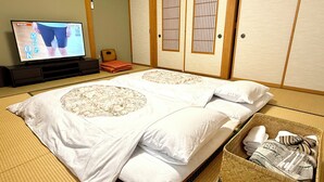 Een traditionele Japanse kamer met tatami vloerbedekking, een futonbed, een televisie en een shoji schuifdeur.