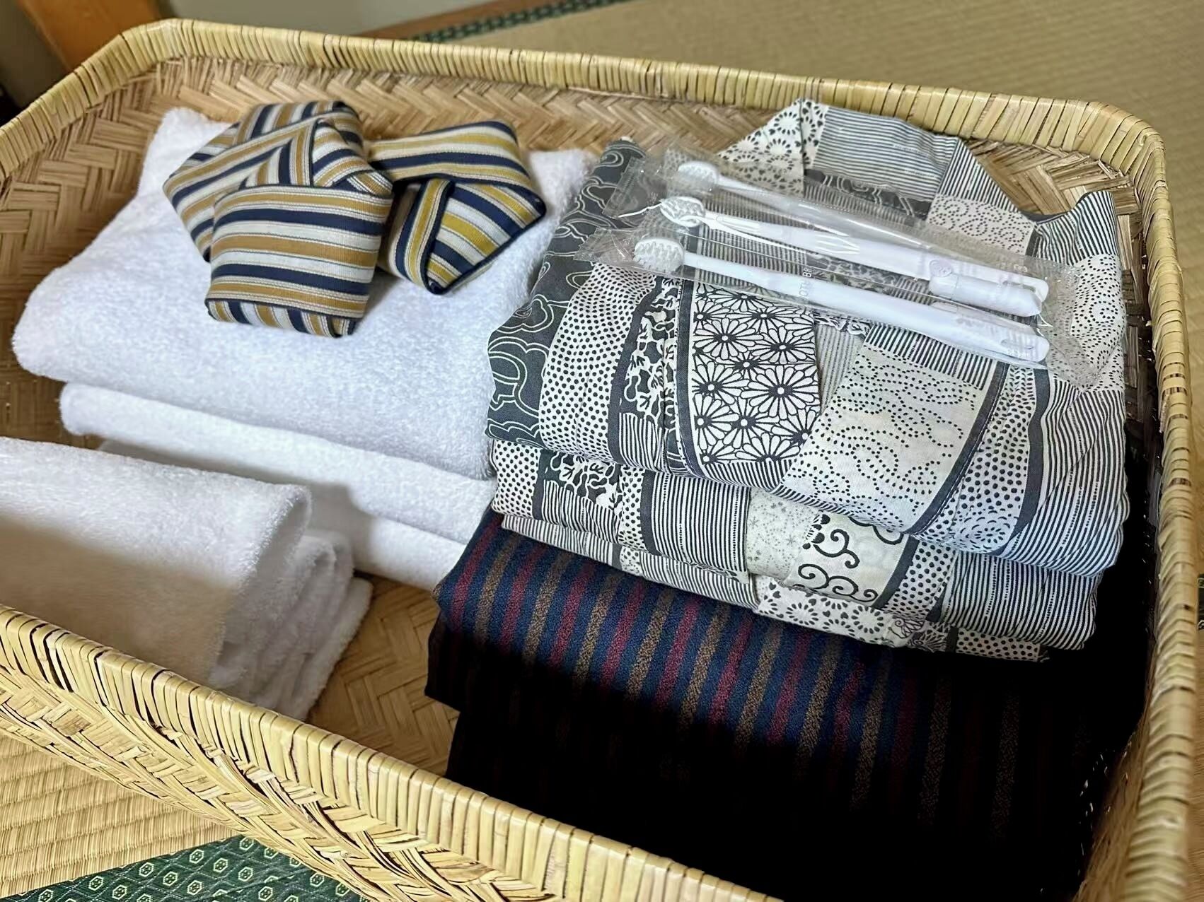 A wicker basket containing folded towels, a striped pillow, and a patterned cloth.