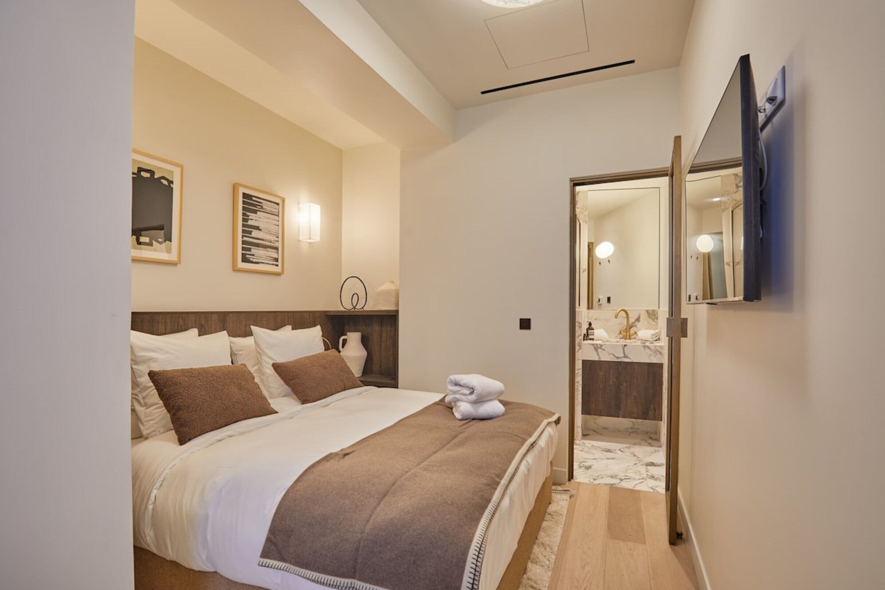Una habitación de hotel con cama, baño con espejo y lavamanos, y obras de arte en las paredes.