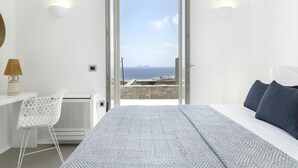 A bedroom with a bed, a chair, a lamp, and a view of the sea. - Pristine Villa With Swimming Pool (Mykonos)
