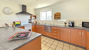 A modern kitchen with a central island, a stove, oven, and dishwasher. There is a window providing natural light and a clock on the wall. - No. 8 - 200m to the best coffee in town and main street (Robe)