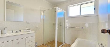 Une salle de bain moderne équipée d’une douche, d’une baignoire, d’un meuble-lavabo avec des tiroirs, d’un grand miroir et d’une fenêtre.