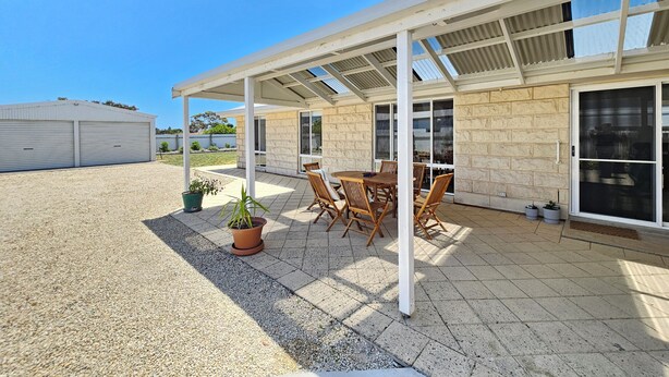A covered patio area with a table and chairs, a potted plant, and a building with large windows and a garage. - No. 8 - 200m to the best coffee in town and main street (Robe)