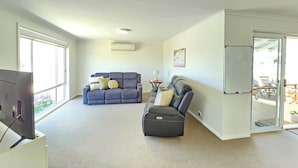A spacious living room with a large window, a grey sofa, a black leather chair, and a flat-screen TV on a stand. - No. 8 - 200m to the best coffee in town and main street (Robe)