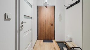 Un couloir avec une porte en bois, un banc, un porte-manteau et un radiateur fixé au mur.