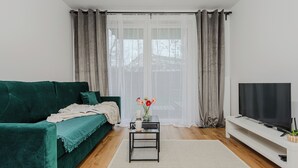 Un salon avec un canapé vert, une table basse, un téléviseur et une fenêtre avec des rideaux.