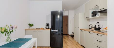 A modern kitchen with white cabinets, a black refrigerator, and a wooden countertop.