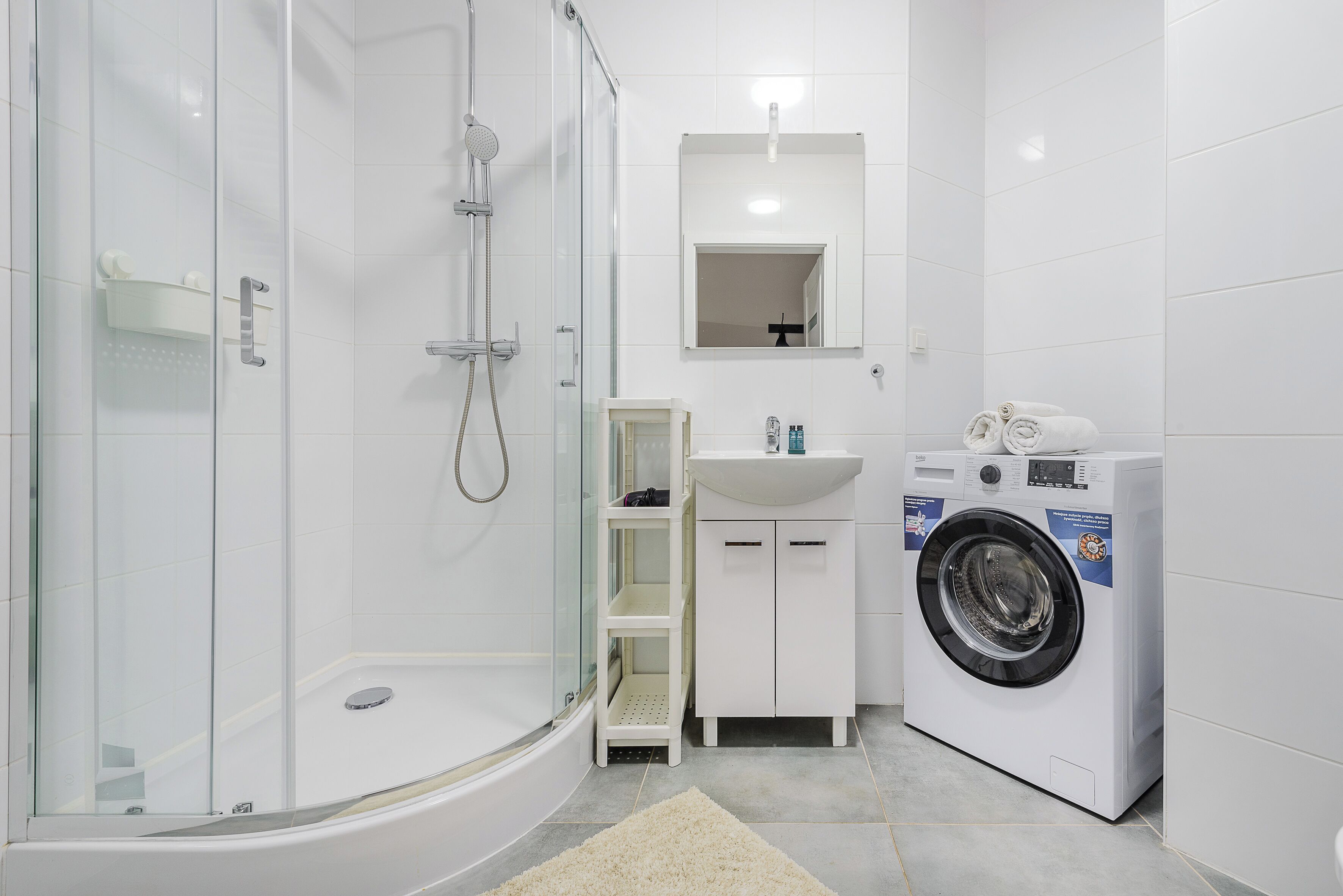A modern bathroom with a glass-enclosed shower, a built-in sink, a washing machine, and a mirror above the sink.