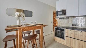 A modern kitchen with white cabinets, a microwave, and an oven. There is a dining table with chairs and a vase of flowers.