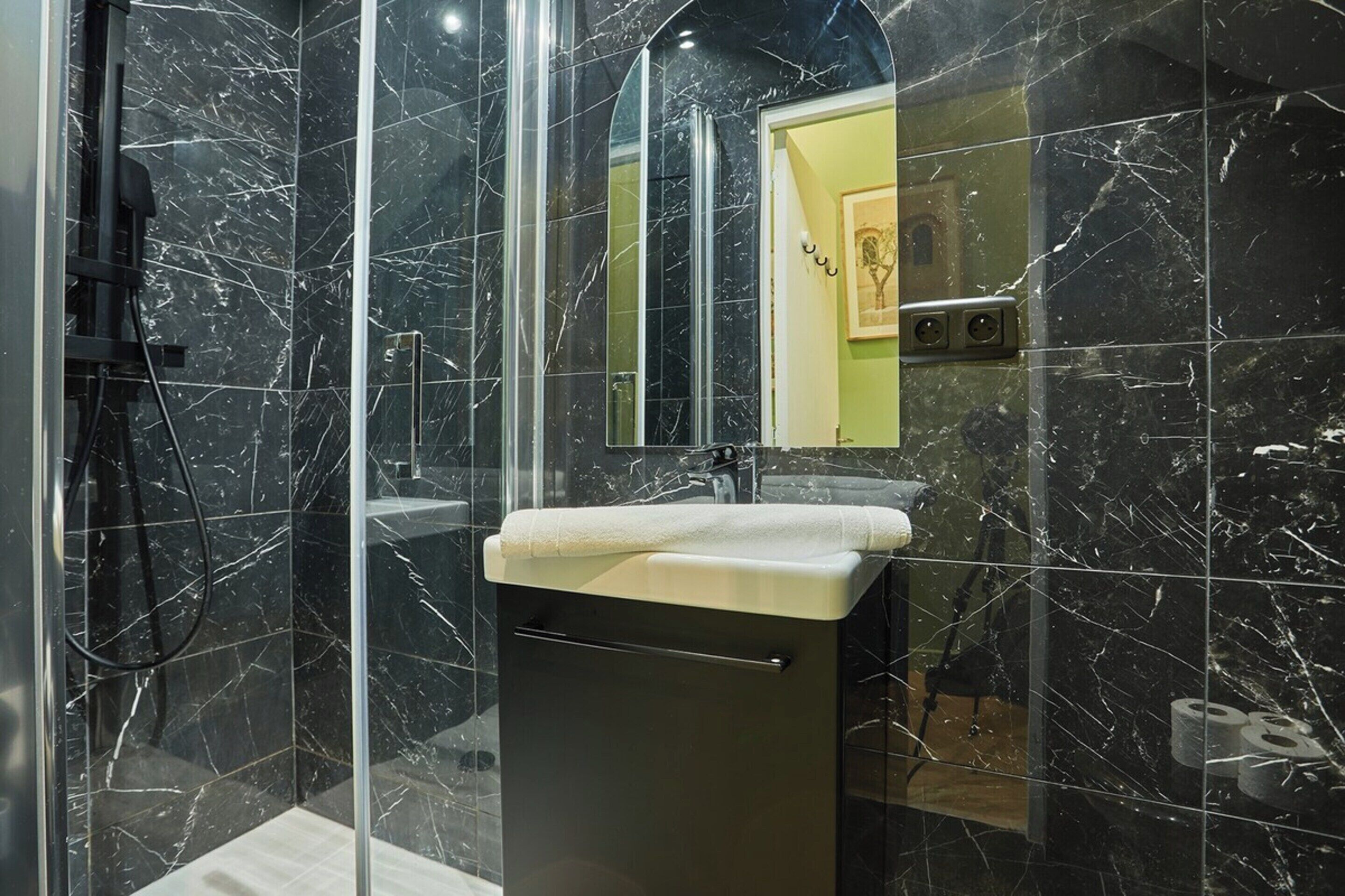 A modern bathroom with a glass-enclosed shower, a marble-tiled wall, and a sink with a towel.