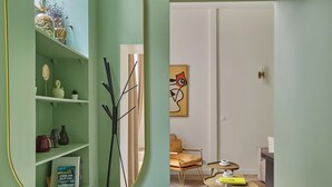 A room with a green wall, a mirror, a bookshelf, a chair, and a table.
