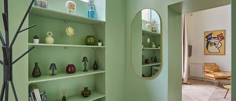 A room with light green walls, a mirrored wall, and shelves with various decorative items.