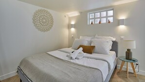 A neatly made bed with white linens and a folded towel, a bedside lamp, and a decorative wall piece.