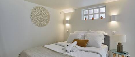 A neatly made bed with white linens and a folded towel, a bedside lamp, and a decorative wall piece.