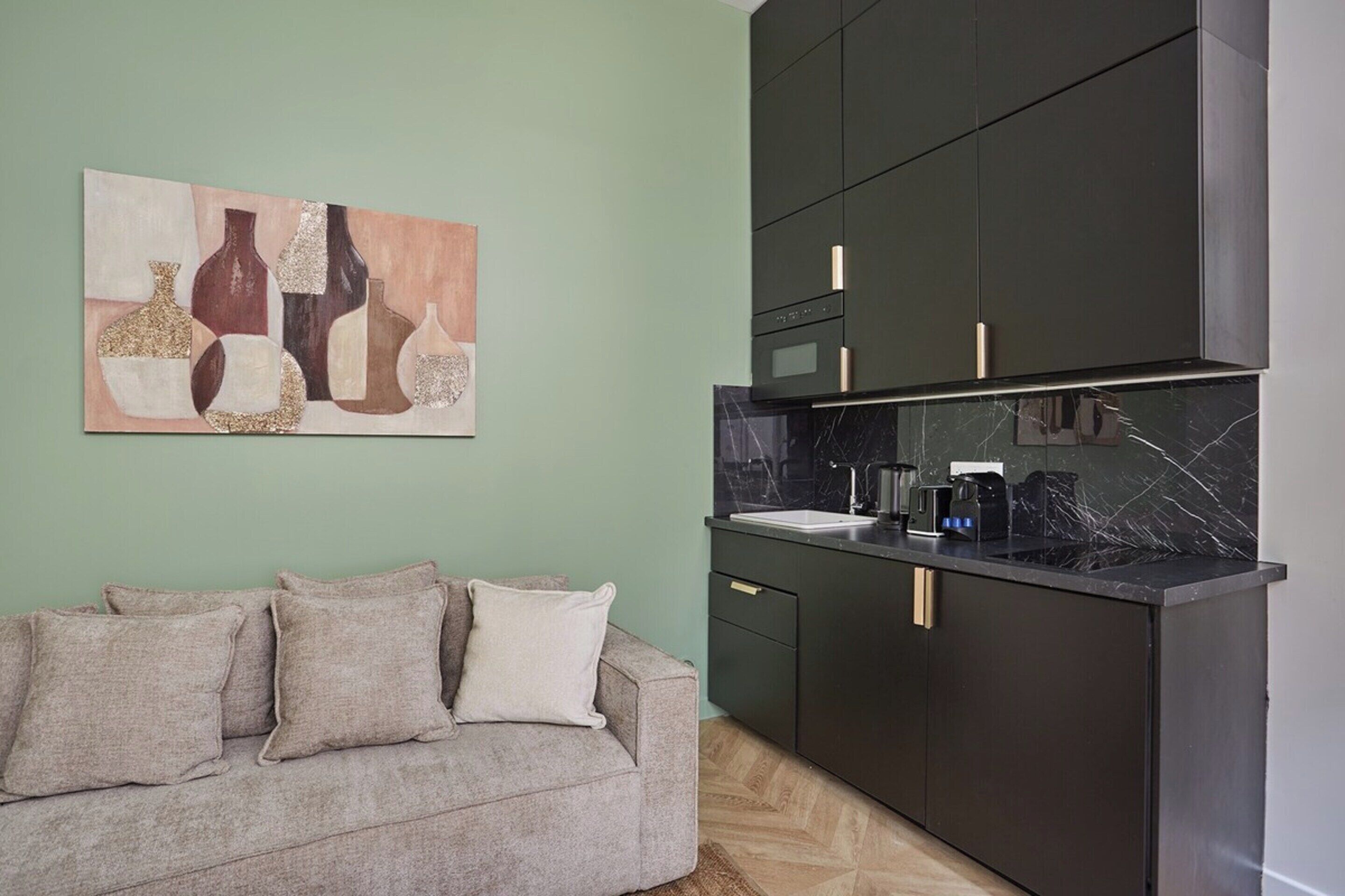 Une cuisine moderne avec des meubles de couleur sombre, un plan de travail en marbre et un tableau accroché au mur.