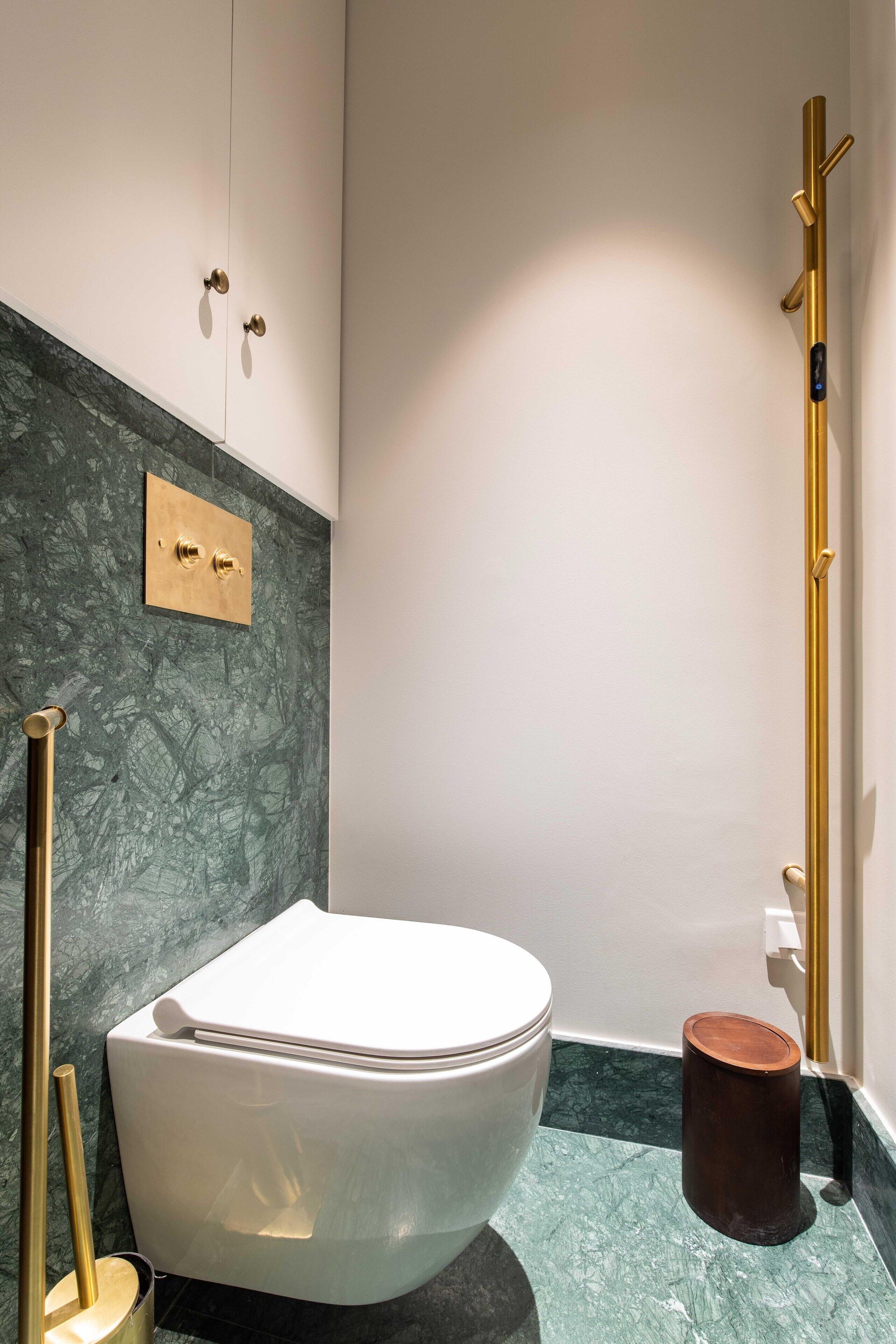 Un baño moderno con inodoro blanco, pared de mármol y grifería dorada.