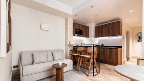Ein modernes Wohnzimmer mit einer Couch, einem kleinen runden Tisch und einem Essbereich mit Holztischen und Stühlen.