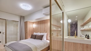 Une chambre moderne comprenant un lit, une armoire en bois, une coiffeuse avec un miroir et une salle de bain avec douche.