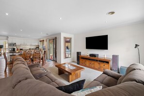 A modern living room with a large sectional sofa, a wooden coffee table, and a flat-screen TV mounted on the wall. - Coastal Family Retreat (Torquay)
