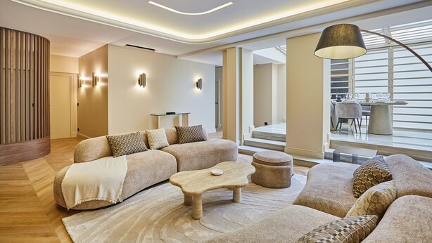 Ein modernes Wohnzimmer mit einer Eckcouch, einem Couchtisch und einer Lampe. Eine Treppe führt zu einer oberen Ebene.