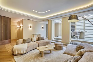 A modern living room with a sectional sofa, a coffee table, and a lamp. There is a staircase leading to an upper level. - Incredible Le Marais Apartment With Terrace (Paris)