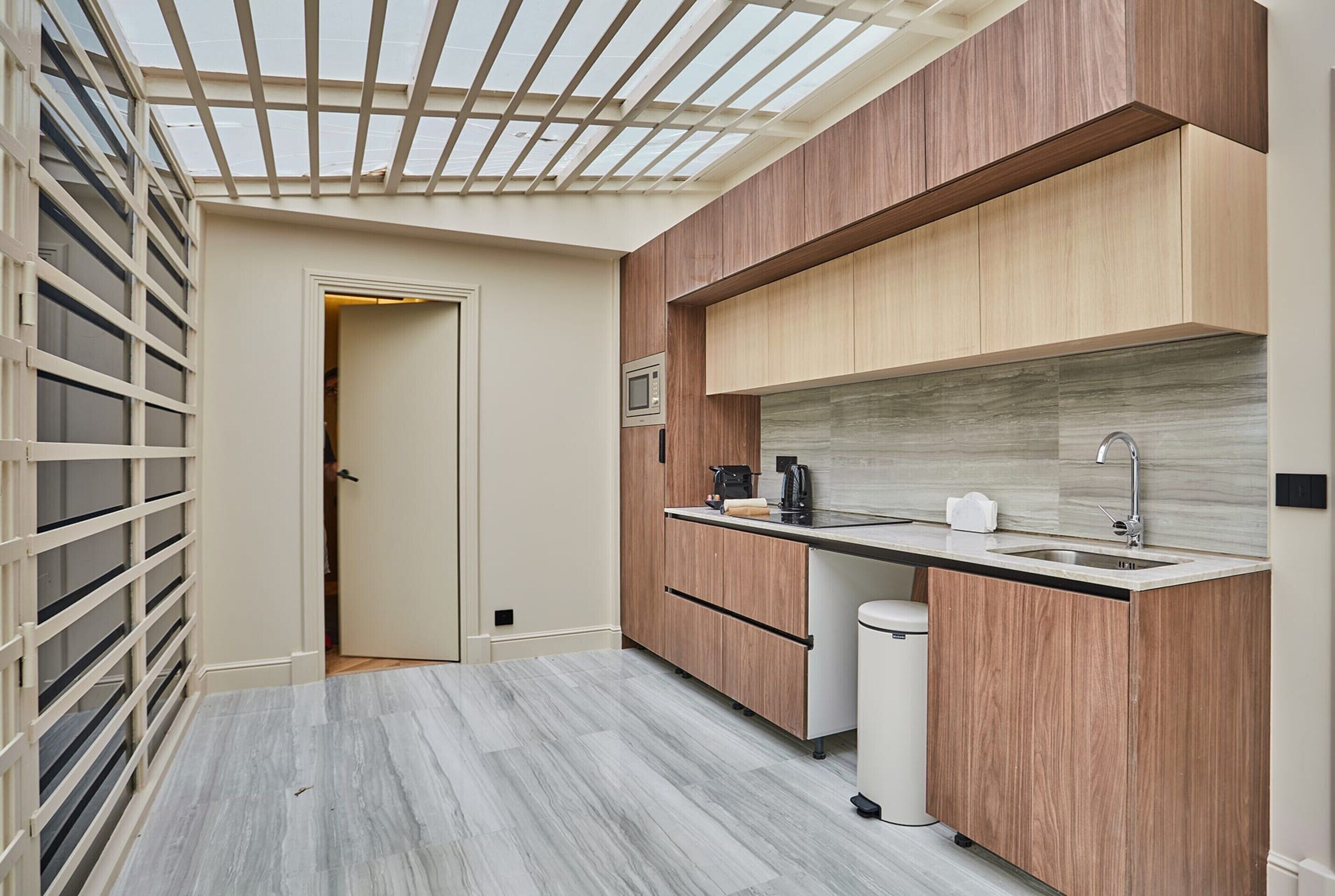 A modern kitchen with wooden cabinets, a marble countertop, and a skylight.