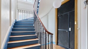 Un escalier aux marches bleues et à la rampe en bois, menant à une pièce dotée d’une porte noire et d’une fenêtre.