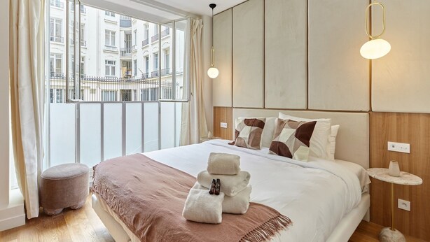 Une chambre d’hôtel moderne avec un grand lit, une vue sur la ville et une petite table ronde avec une lampe.