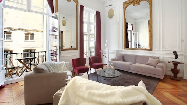 Amplia sala de estar con sofá, sillones, una mesa de centro y un balcón con mobiliario exterior.
