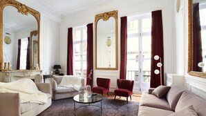 Un salón amplio con un sofá color beige, un sillón rojo y un espejo grande con un marco decorativo.