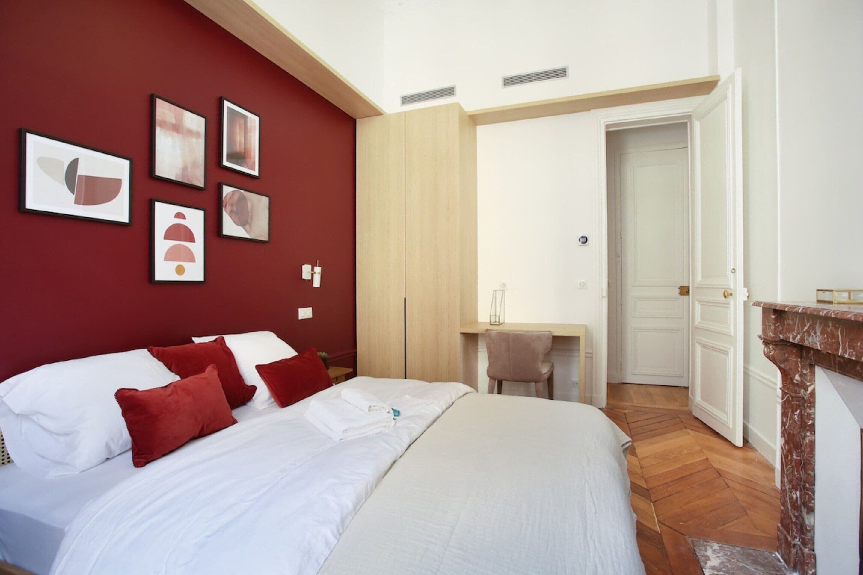 Une chambre d’hôtel avec un grand lit, des murs rouges, une armoire en bois, un bureau et une cheminée.