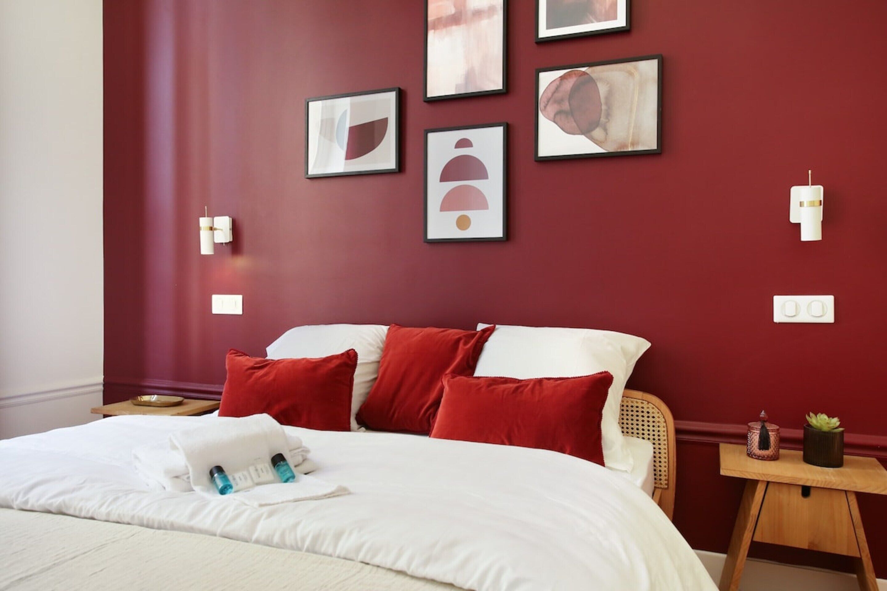 A hotel room with a large bed, red pillows, and artwork on the wall.