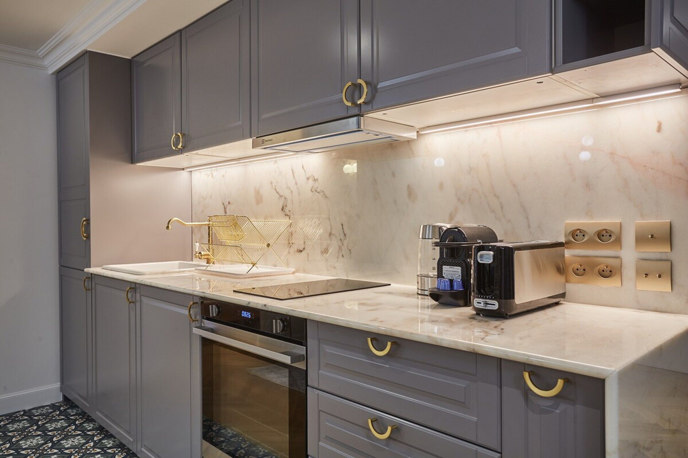 A modern kitchen with grey cabinets, a marble countertop, a built-in oven, and a coffee machine.