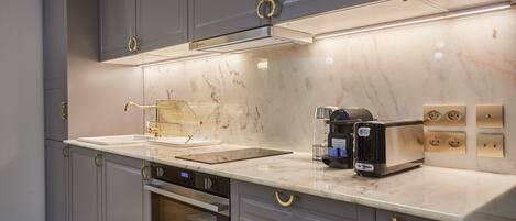 A modern kitchen with grey cabinets, a marble countertop, a built-in oven, and a coffee machine.