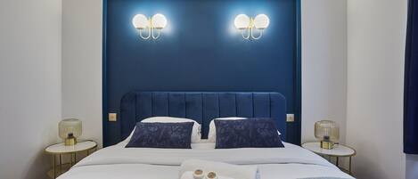 Un lit bien fait, avec une tête de lit bleue, deux lampes de chevet et un ensemble de produits de toilette posés sur le lit.