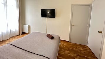 Un dormitorio con una cama, un televisor montado en la pared, un radiador y un equipo de aire acondicionado.