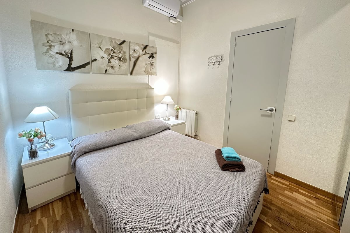 Quarto com cama, mesa de cabeceira, abajur e decoração na parede.
