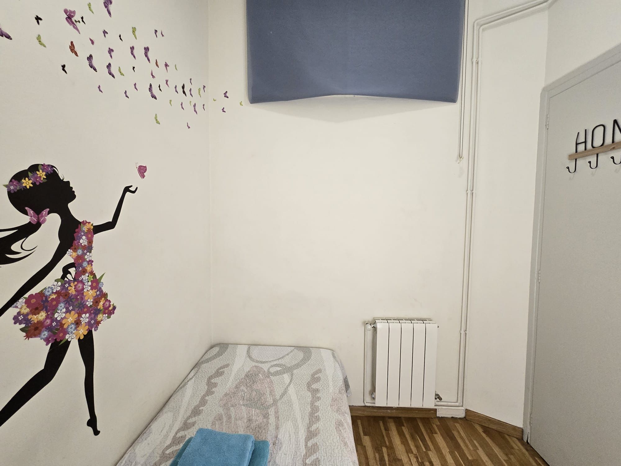 Un dormitorio con una cama, un radiador y una decoración de pared que muestra a una niña con flores.