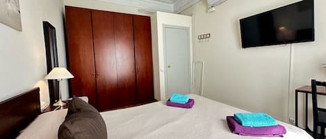 A hotel room with a bed, a TV, a wardrobe, and a bedside table with a lamp.