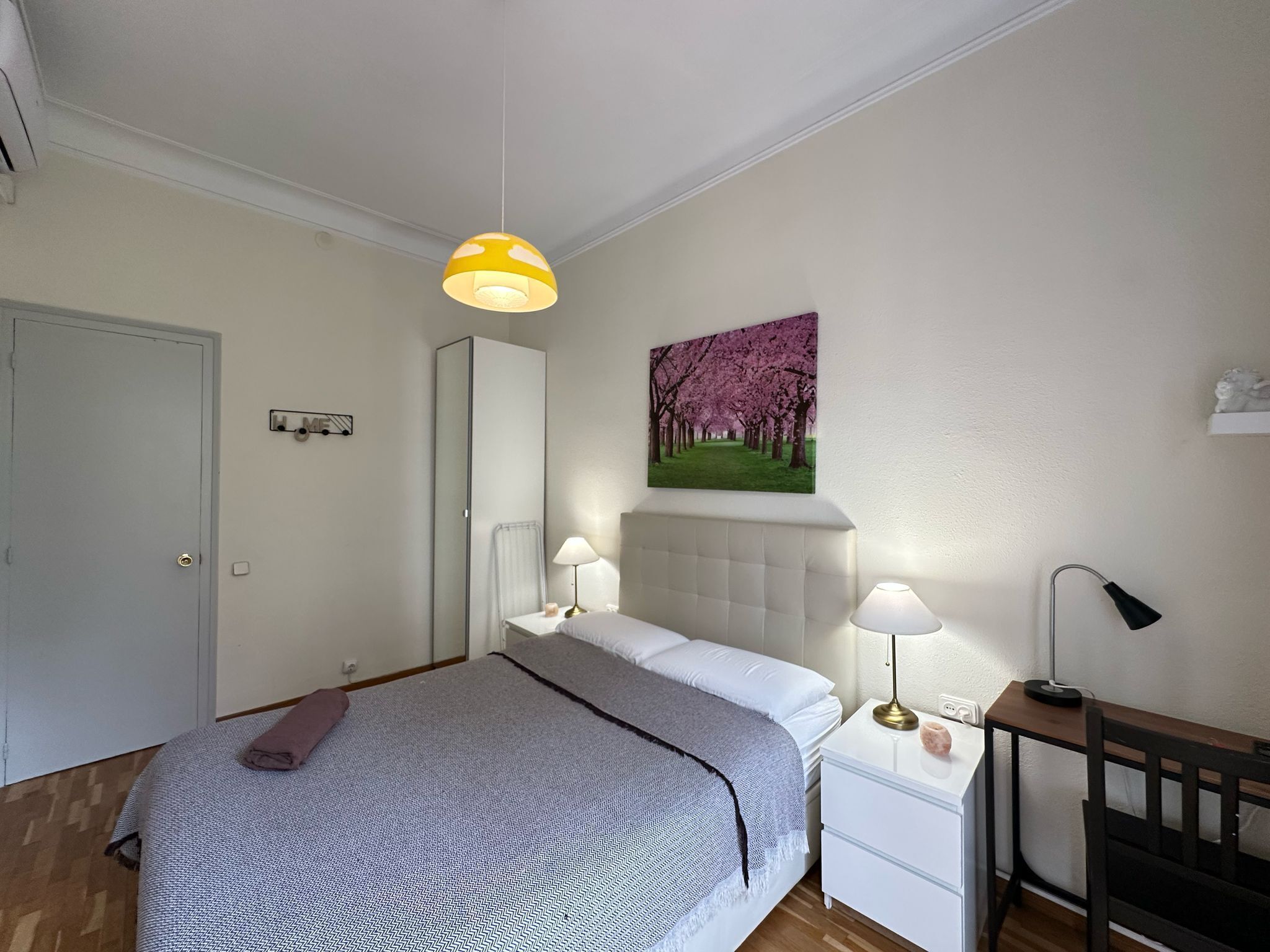 A bedroom with a bed, bedside tables, a lamp, a painting, and a door.