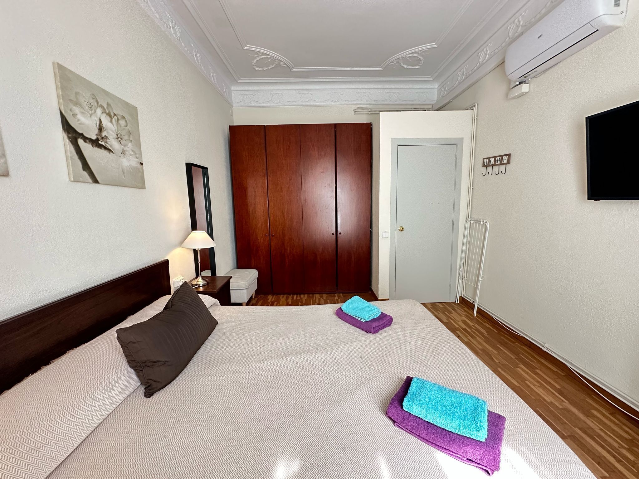 Ett hotellrum med en säng, ett nattduksbord, en lampa, en garderob, en spegel, en tv och en skylt med texten ”HEM”.