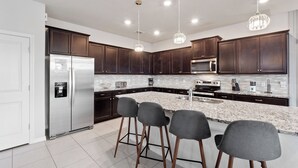 A modern kitchen with dark wood cabinets, stainless steel appliances, a marble countertop, and bar stools.