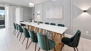 A modern dining room with a long white table, teal chairs, and a chandelier.