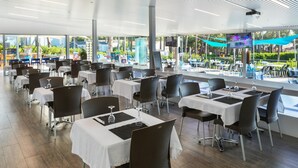A modern restaurant with multiple tables and chairs, large windows, and a view of the outdoors. - Bungalow Near Pals Beach & Pool (Pals)